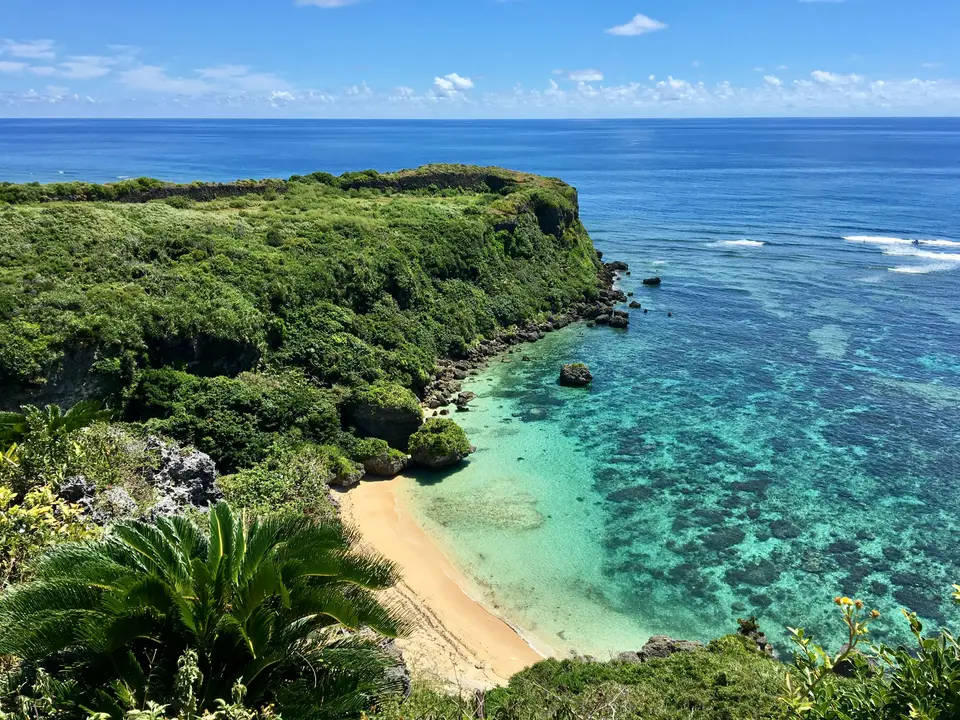 沖繩的白沙灘和海邊綠色灌木｜<a href="https://unsplash.com/photos/a-beach-with-a-sandy-beach-and-green-bushes-JdE62Hcw8x4" target="_blank" rel="noopener">Unsplash 原圖</a>