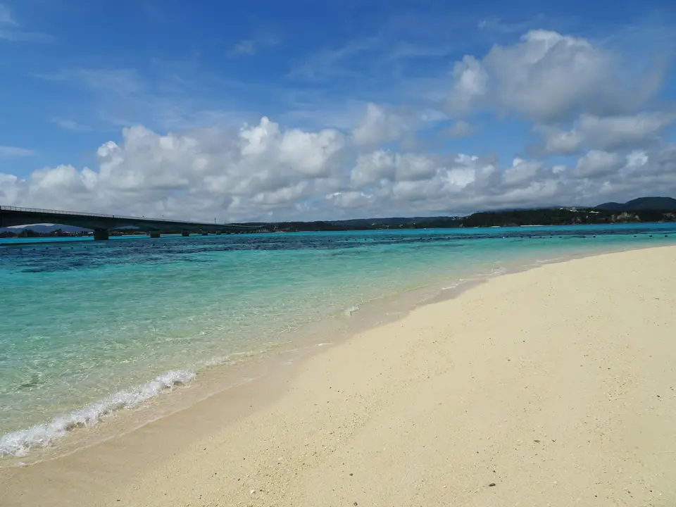 古宇利海灘的清澈海水，遠方有跨海大橋｜<a href="https://unsplash.com/photos/a-sandy-beach-with-clear-blue-water-and-a-bridge-in-the-distance--lH8Ihr8qms" target="_blank" rel="noopener">Unsplash 原圖</a>