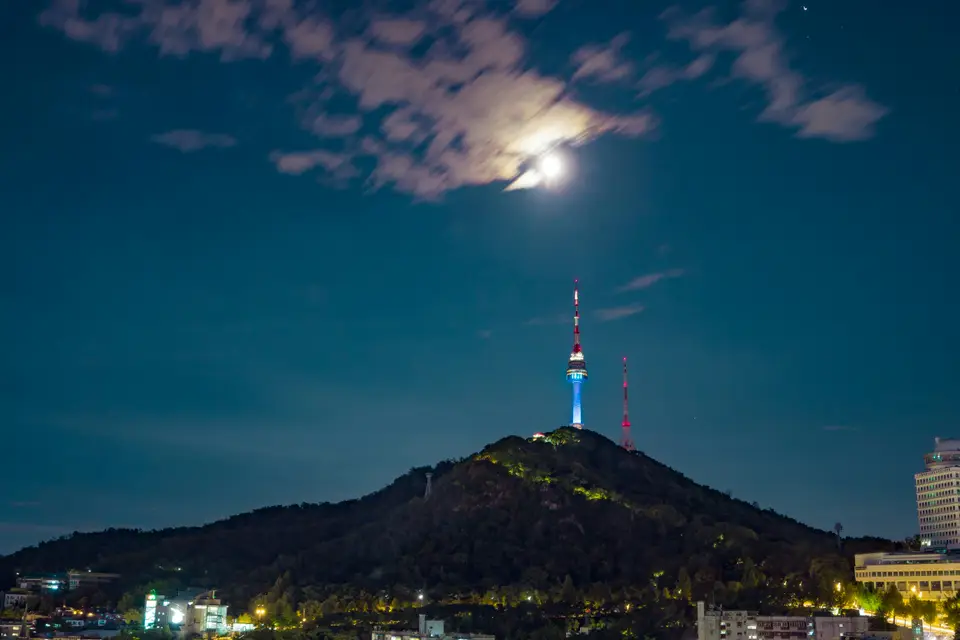 月亮升起，南山上的 N 首爾塔和城市夜景｜<a href="https://unsplash.com/photos/a-full-moon-rising-over-a-city-with-a-mountain-in-the-background-8dR9ZEF6EFU" target="_blank" rel="noopener">Unsplash 原圖</a>